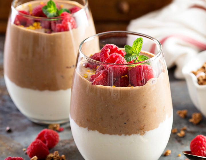 Glass of yogurt layered with chocolate and topped with raspberries