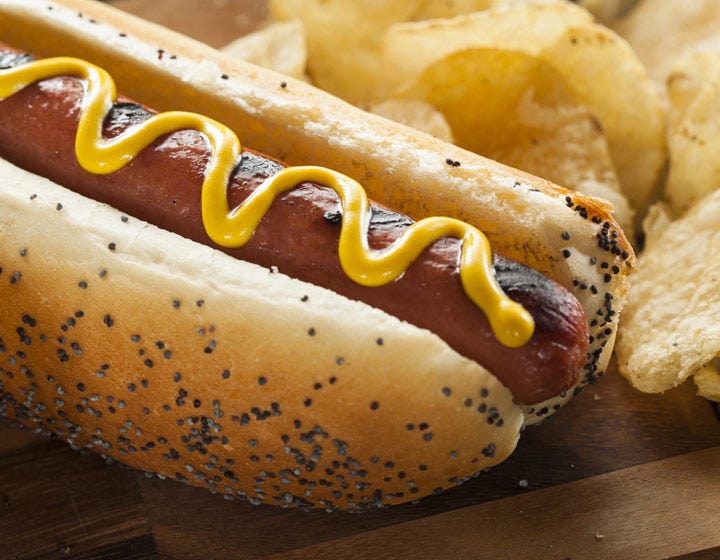 Hot dog with mustard on a seeded bun, illustrating benefits of starches in processed meat