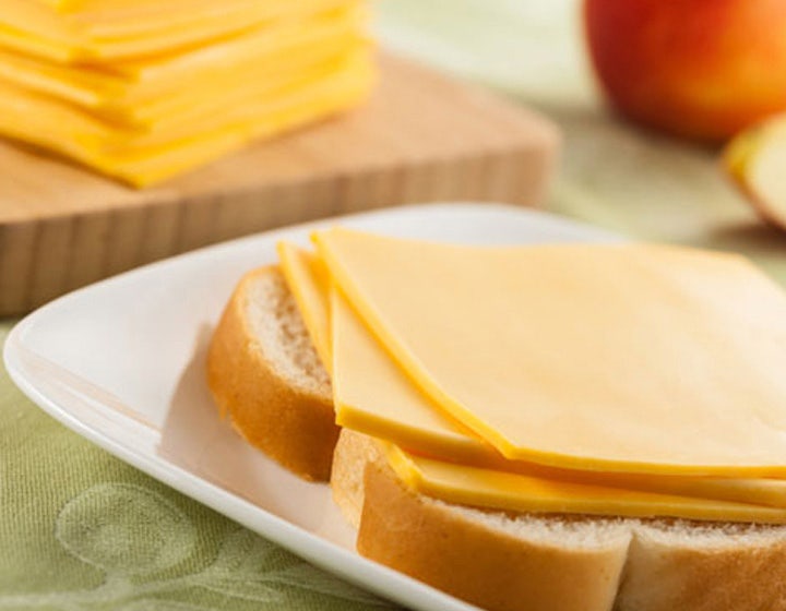 Slices of yellow cheese stacked on a white plate, representing dairy cheese innovations