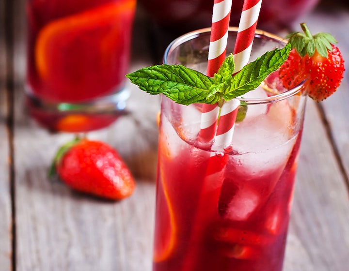 Red drink with ice in a glass, garnished with fresh mint and a strawberry