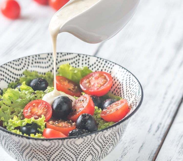Creamy salad dressing being poured on salad, representing egg-free emulsified dressings